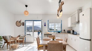 Una cocina moderna con armarios blancos, un comedor con sillas de mimbre y vistas a las montañas a través de la ventana.