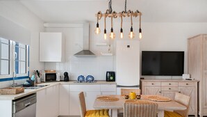 Cocina moderna con armarios blancos, una isla central y un comedor con sillas de mimbre y cojines amarillos.