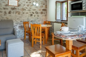 Une pièce chaleureuse avec un mur en pierre, un canapé gris, des chaises en bois, une petite table avec une tasse et un verre, et un four à micro-ondes placé au-dessus de la table.
