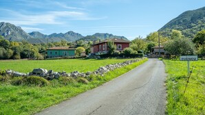 A rural road with houses, a stone wall, and mountains in the background.