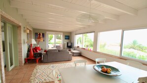 A living room with a sofa, TV, and dining table with fruit. - Holiday Home 'Villa Betty' with Sea View, Wi-Fi and Air Conditioning (Dénia)