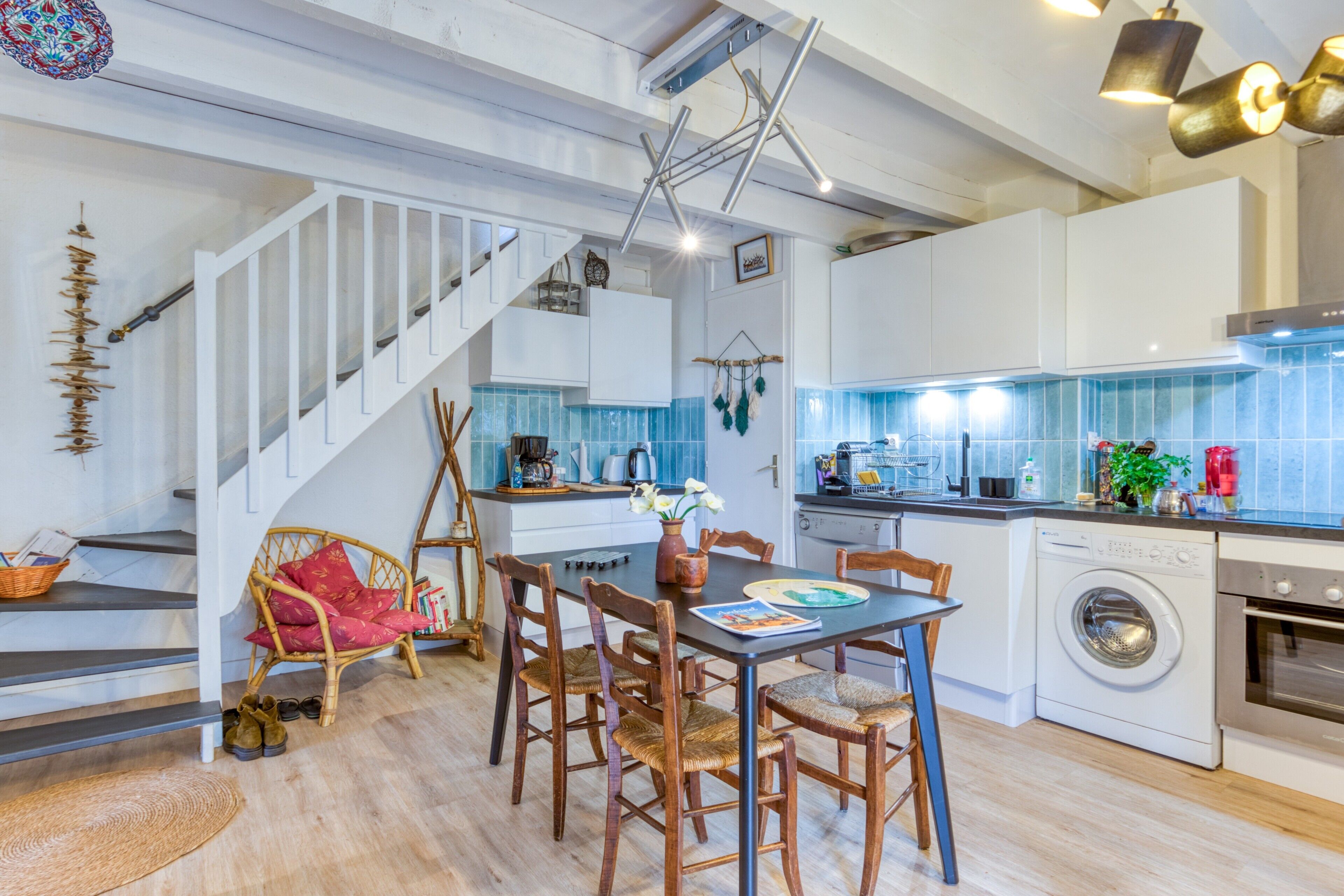 A modern kitchen with white cabinets, a built-in washing machine, and a dining area with wooden chairs and a table.