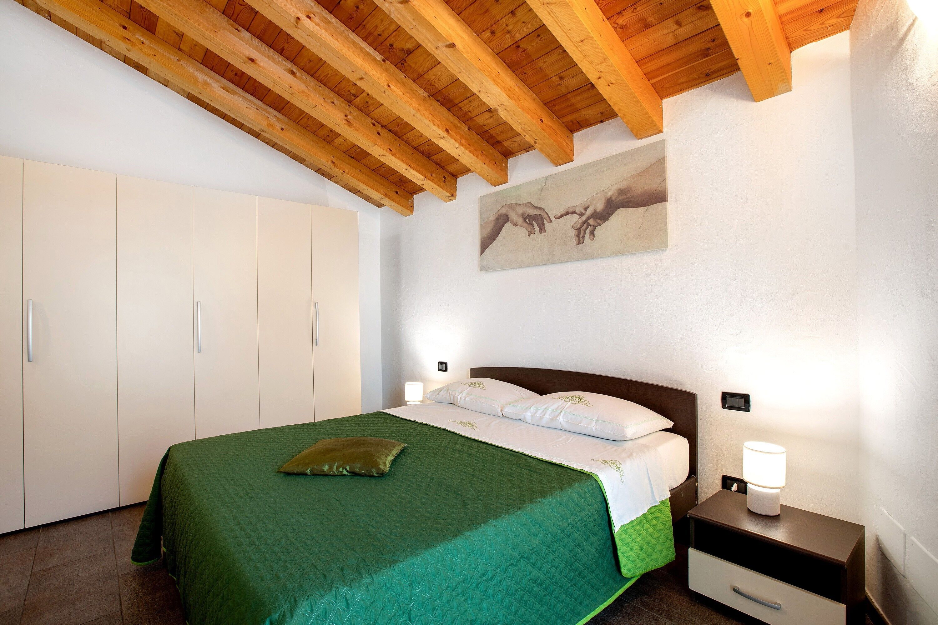 A bedroom with a bed, nightstands, a wooden ceiling, a painting, and a wardrobe.