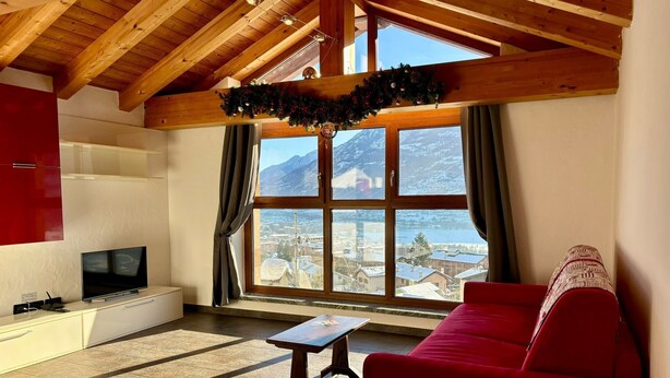 Un salon avec un canapé rouge, un téléviseur, un plafond en bois et une grande fenêtre donnant sur la montagne.