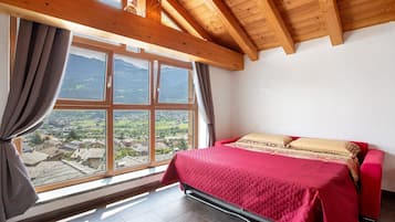 A bedroom with a bed, a window with curtains, and a view of a mountainous landscape.