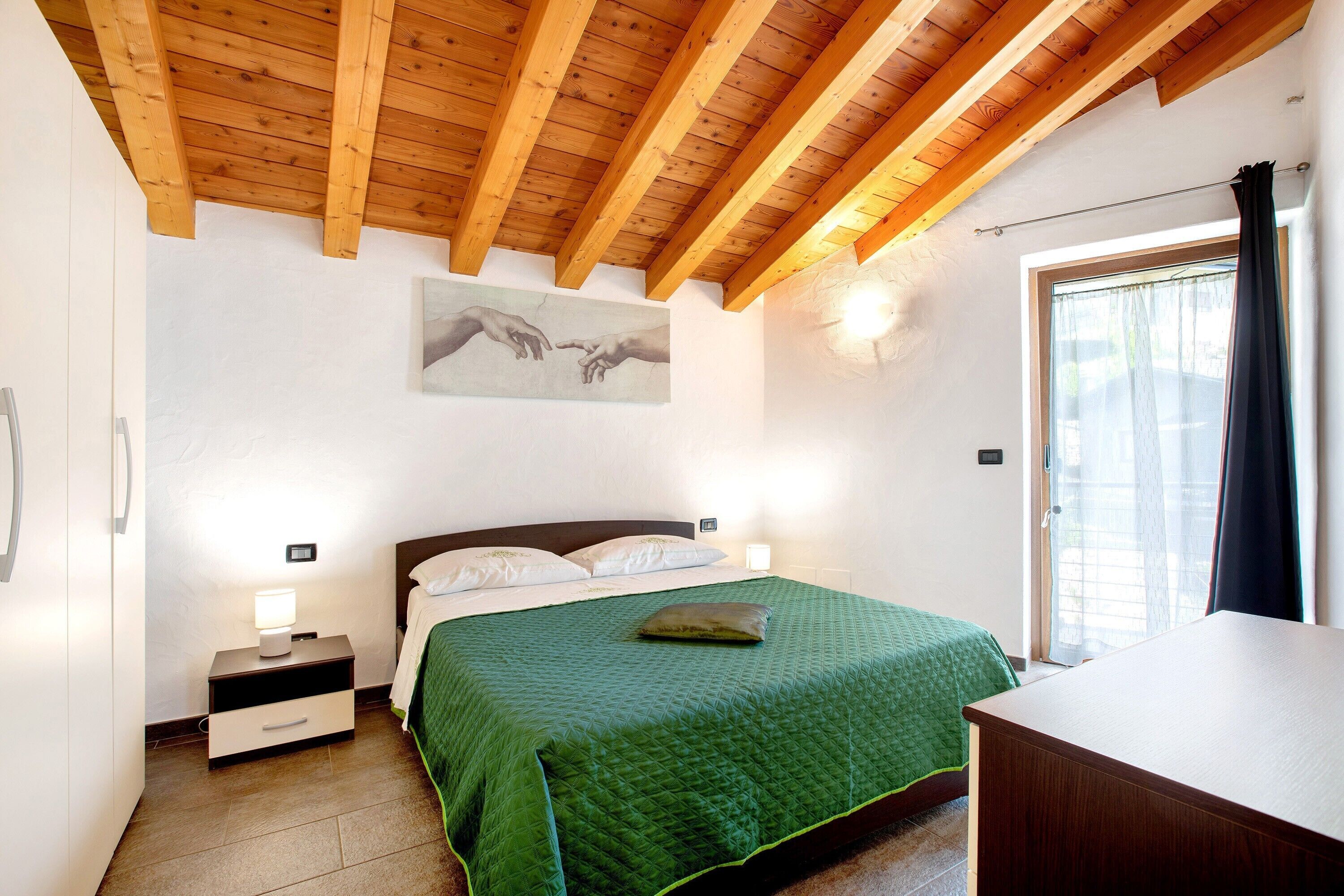 Ein Schlafzimmer mit Holzbalkendecke, einem Bett mit grüner Steppdecke, Nachttischlampen und einem Bild an der Wand.