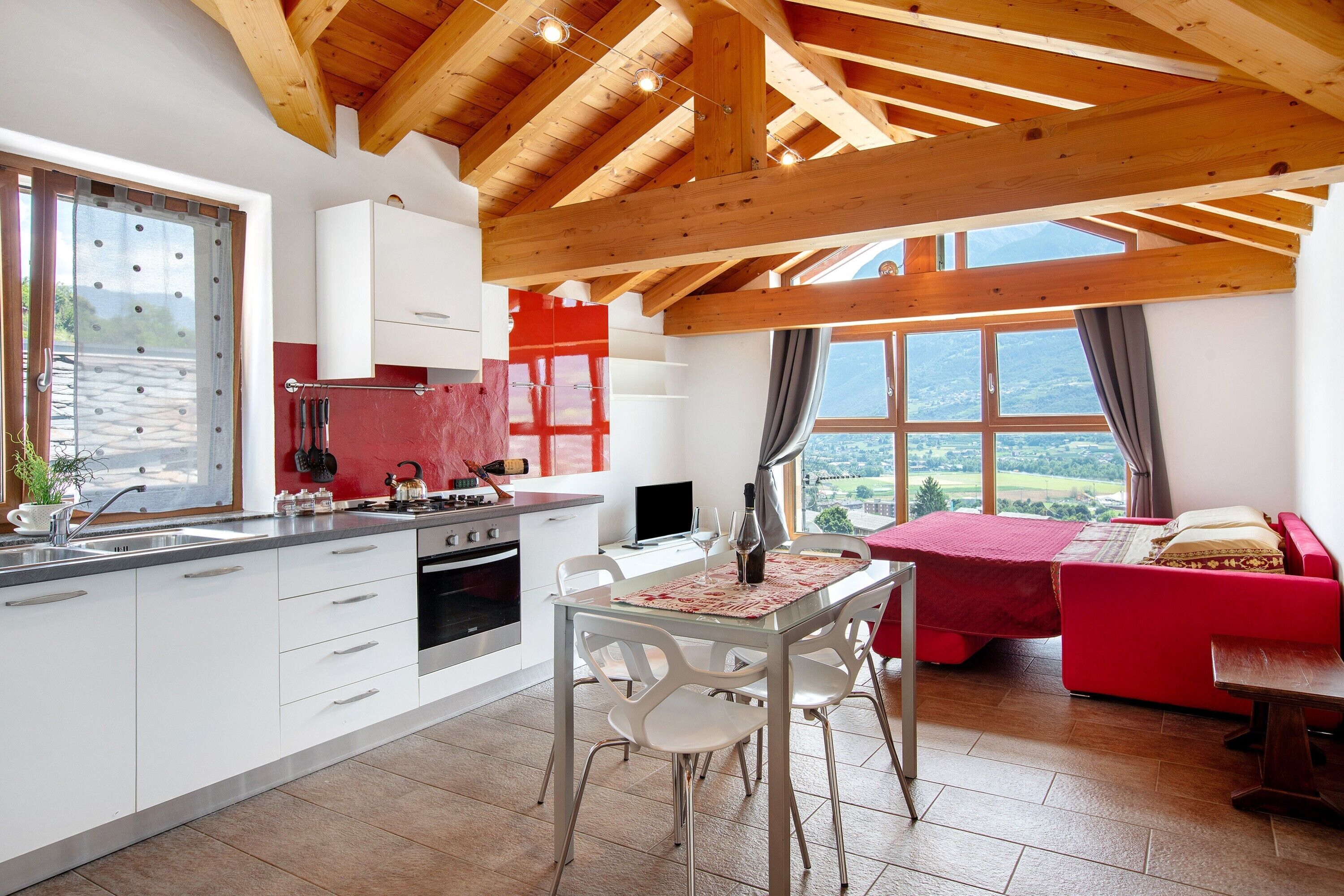 A modern kitchen with a dining area, a red sofa, and a view of the outdoors.