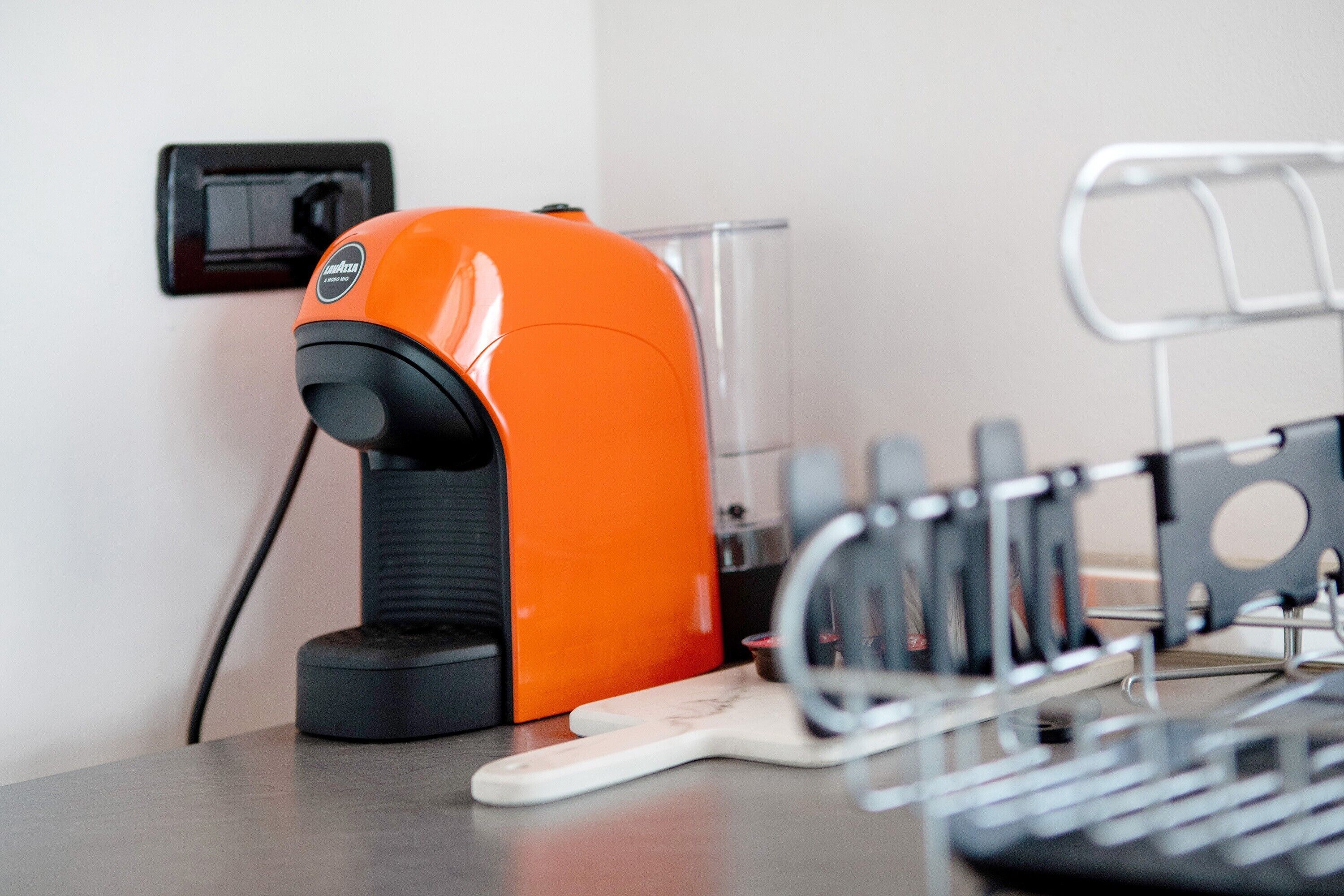 A coffee machine, a power outlet, and a metal rack with items on a countertop.
