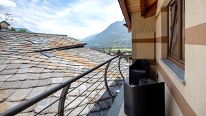 Un balcon doté d’un toit en pierre, d’une rambarde en métal et offrant une vue sur les montagnes.