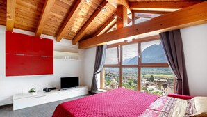 Une chambre avec un grand lit, une télévision, une commode blanche et une fenêtre donnant sur les montagnes.