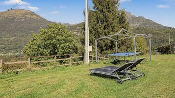Un'area verde all'aperto con un gazebo in metallo, un tavolo con rivestimento blu e due lettini da sole.