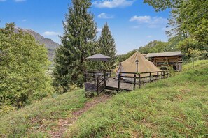 Un camping con una tienda de campaña, una terraza de madera y montañas al fondo.