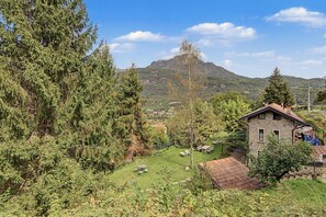 Paisaje rural con una casa de piedra, un campo cubierto de hierba y una montaña al fondo.