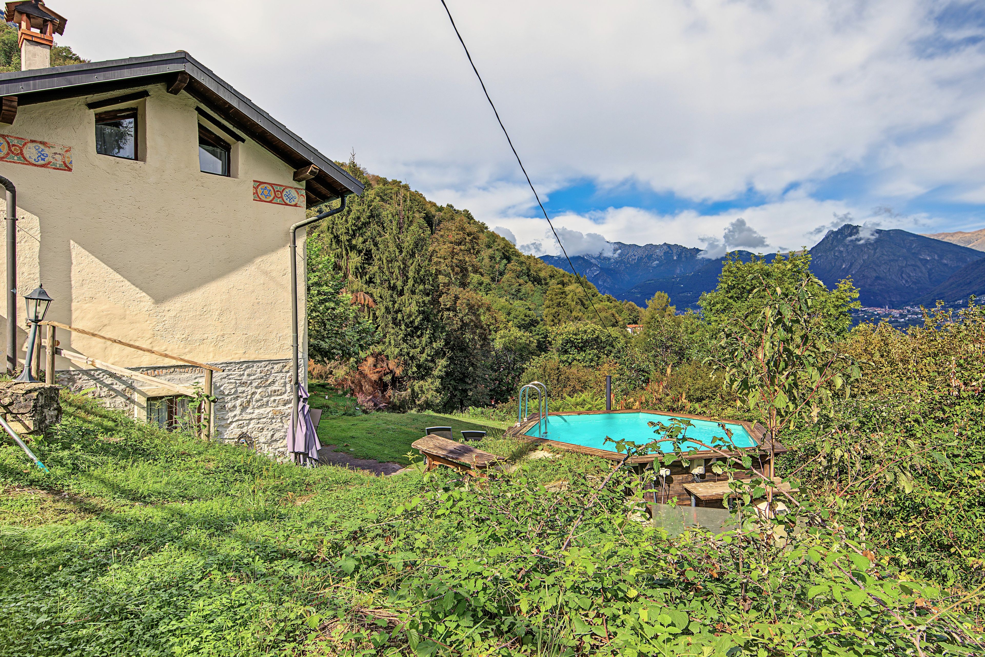 Una casa con un muro in pietra, un patio in legno e una piscina immersa nel verde.