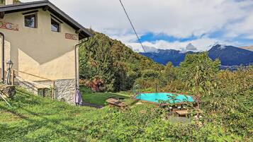 Una casa con un muro in pietra, un patio in legno e una piscina immersa nel verde.