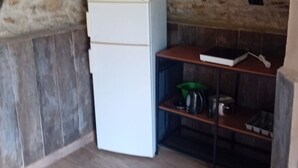 Una habitación con techo de piedra, un refrigerador blanco y una estantería de madera con utensilios de cocina.