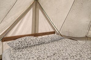 Una carpa con estructura de madera y una cama con ropa de cama estampada.