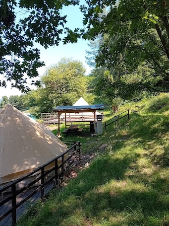 A tent, a wooden structure with a roof, and a bench in a grassy outdoor setting.