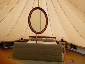 A tent with a bed, a round mirror, and a nightstand with a lamp.