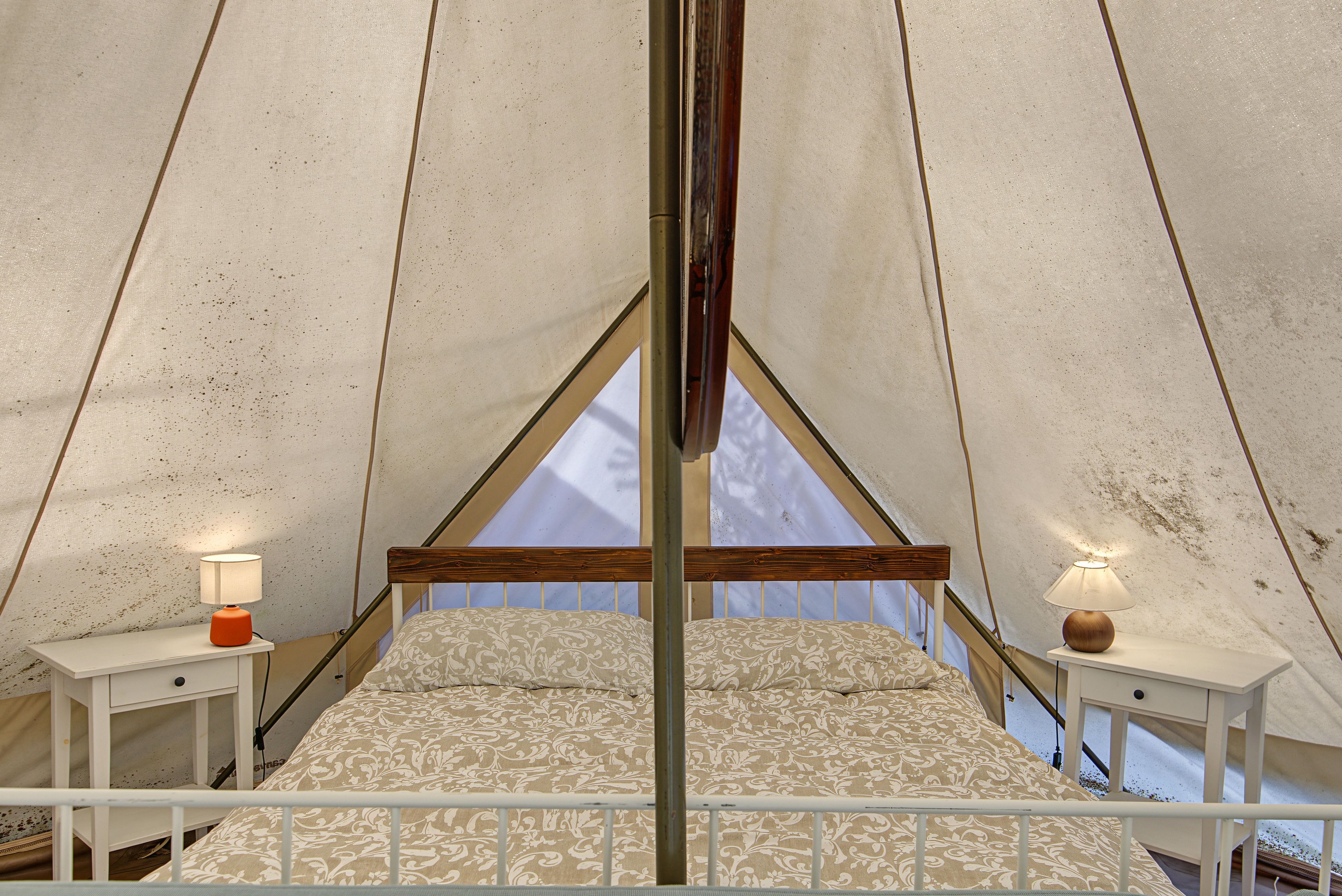 Alojamiento en tienda de campaña con cama, dos mesitas de noche y vistas a través de la ventana.