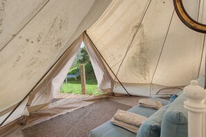A tent interior with a view of a grassy area and a tree.