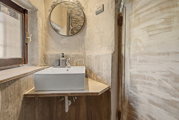 Un baño con un lavamanos blanco, tocador de madera, un espejo redondo y un interruptor de luz en la pared.