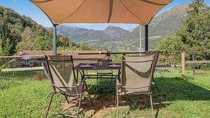 Un espace de restauration en plein air, avec une table et des chaises disposées sous une tonnelle, offrant une vue sur un paysage montagneux.