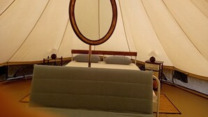 Ein Zelt mit Bett, einem runden Spiegel und einem Nachttisch mit Lampe.