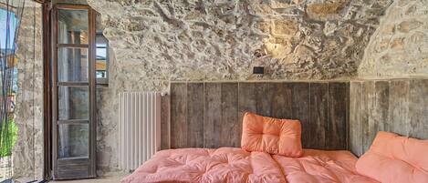 Un dormitorio con techo de piedra, estructura de cama de madera y colcha rosa.