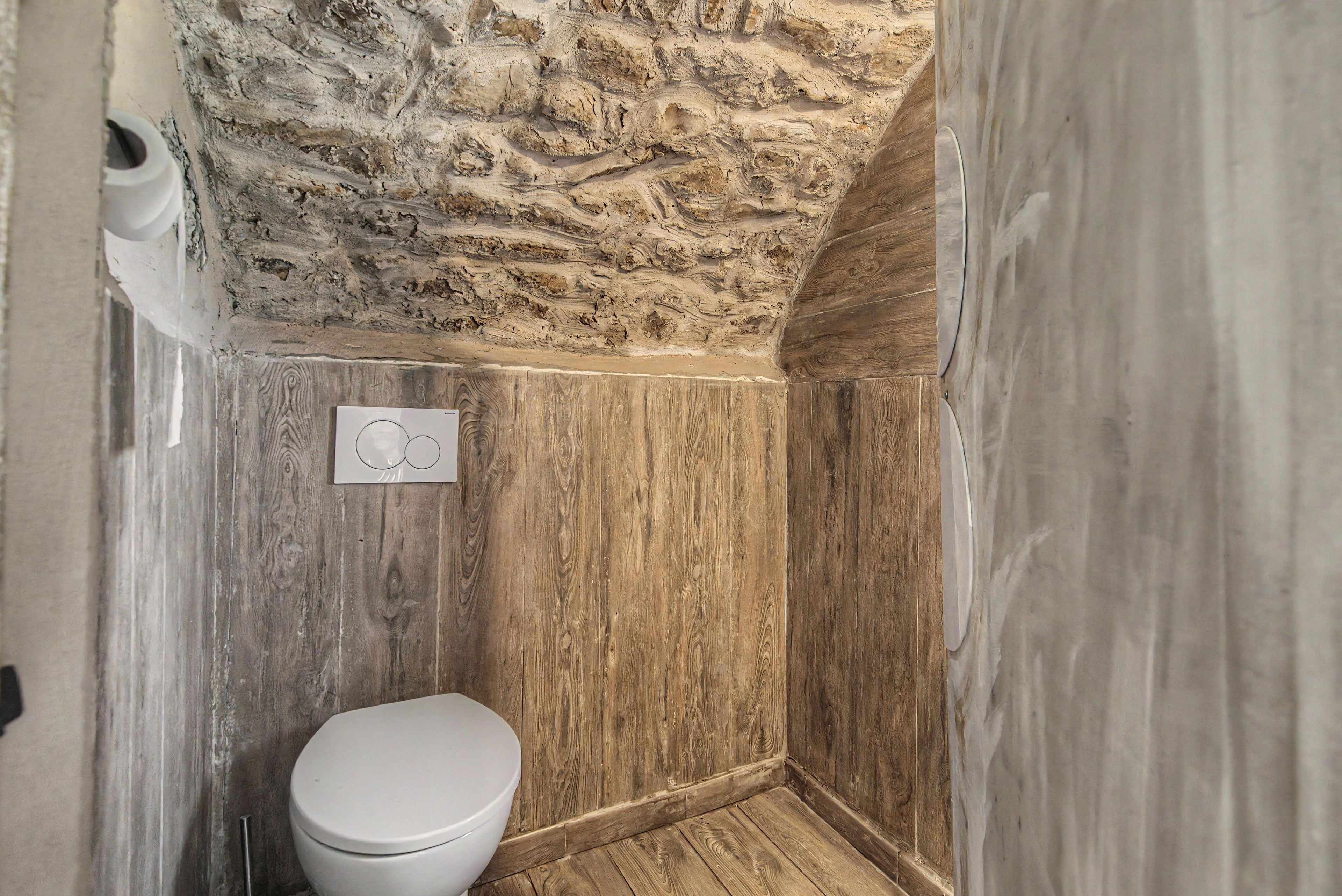 Een kleine, smalle badkamer met een stenen muur, houten lambrisering en een wit toilet.