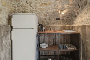 A compact kitchen with a white refrigerator, a wooden shelf, and a metal rack with dishes.