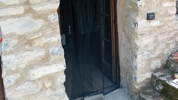 Ein Eingang zu einem Steinhaus mit einem ‚Welcome‘-Schild, einer Laterne und einer Tür mit schwarzem Vorhang.