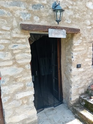 A stone building entrance with a 'Welcome' sign, a lantern, and a door with a black curtain.