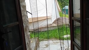Une porte qui mène à une zone abritée par une tente, d’où l’on peut admirer un paysage verdoyant.