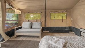 Une pièce aménagée comme une tente, avec un lit, un canapé et une fenêtre donnant sur un paysage verdoyant.