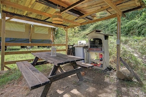 En utomhuskonstruktion av trä med ett picknickbord och en grill.