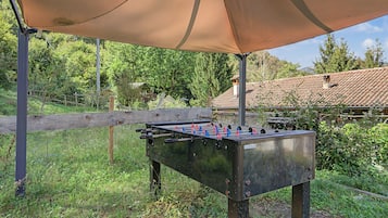 Ein Tischkicker im Freien unter einer Markise, umgeben von Pflanzen und einem Holzzaun.