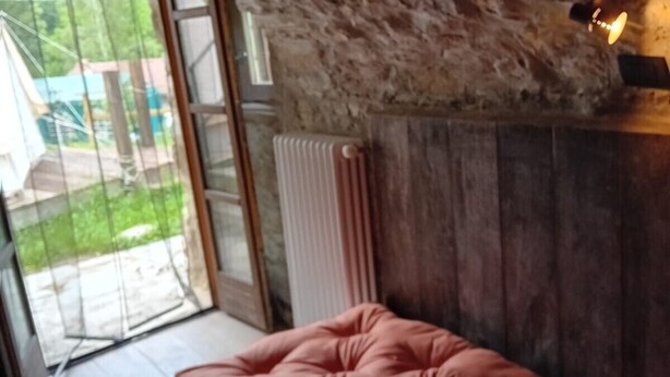 Une pièce avec un plafond en pierre, un lit agrémenté d’un coussin rouge, une armoire en bois et une vue sur l’extérieur, visible à travers une porte vitrée.