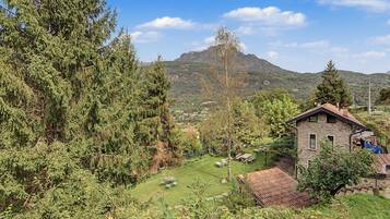 Ländliche Landschaft mit einem Steinhäuschen, einer Wiese und einem Berg im Hintergrund.