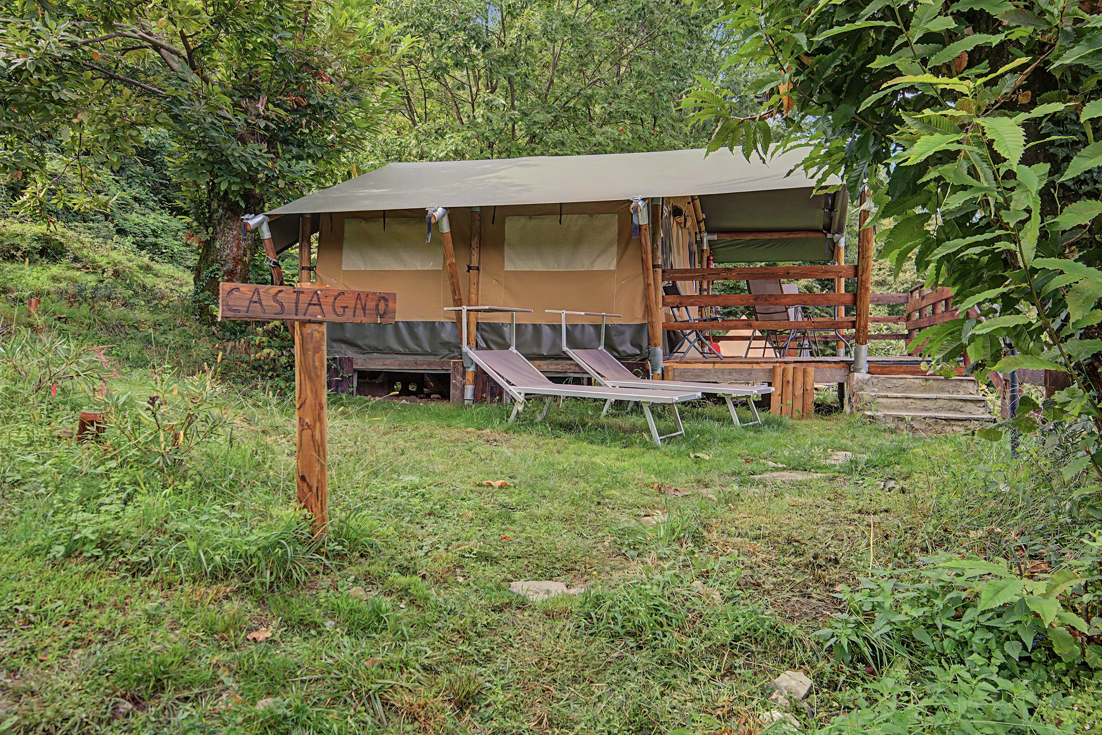 Ein rustikaler Campingplatz mit einer Holzhütte, einem Schild mit der Aufschrift 'CASTAGNO' sowie einem Tisch und Stuhl.