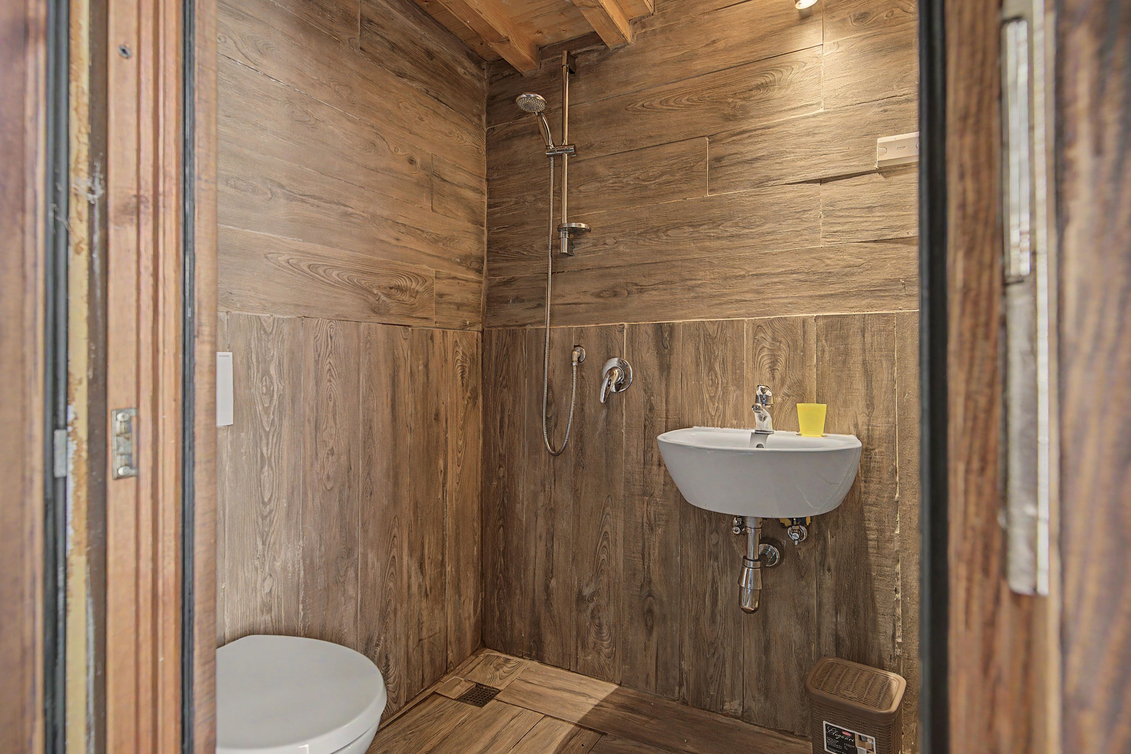 Une petite salle de bain aux murs lambrissés, équipée de toilettes, d’un lavabo et d’une douche.
