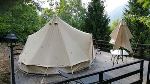 Un espace aménagé sous une tente, avec une table et des chaises, entouré d’une terrasse en bois et de verdure.