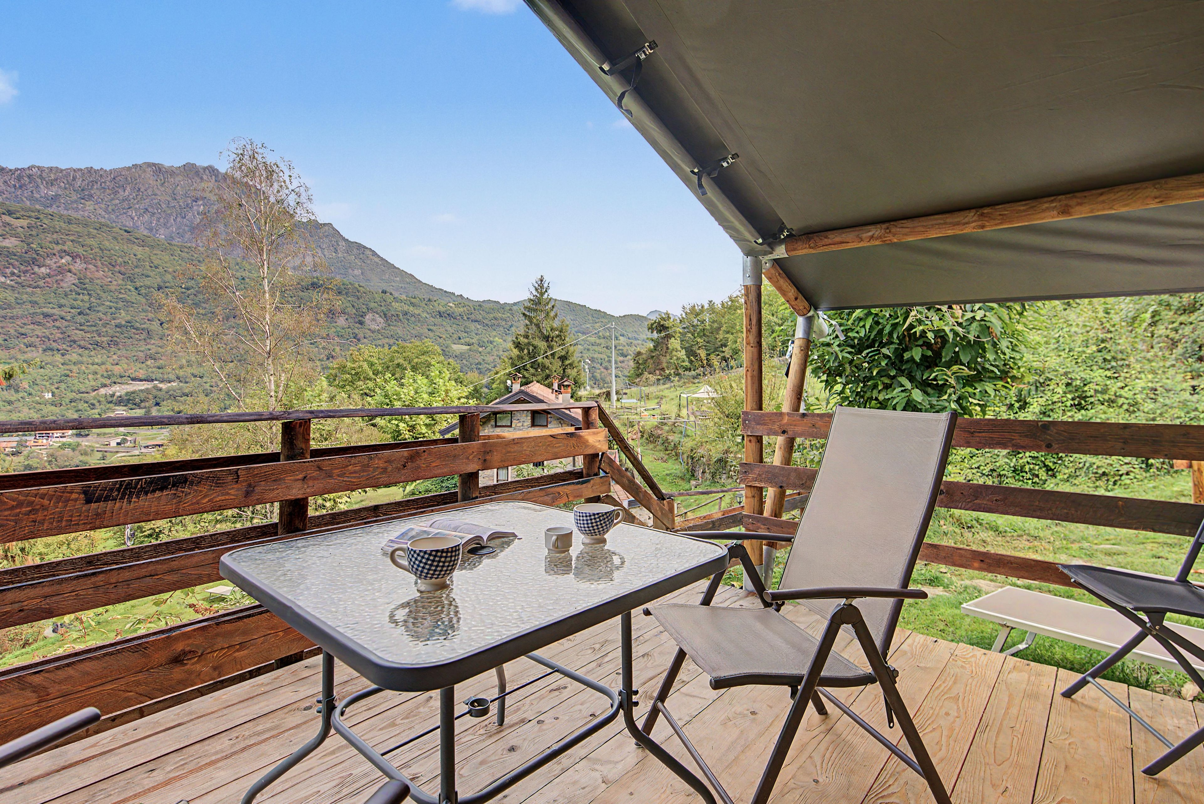 Eine Holzterrasse mit Tisch und Stühlen, mit Blick auf eine gebirgige Landschaft.