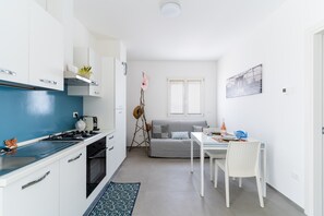 Une cuisine de taille réduite avec des meubles blancs, une cuisinière et un coin repas comprenant une table et des chaises.