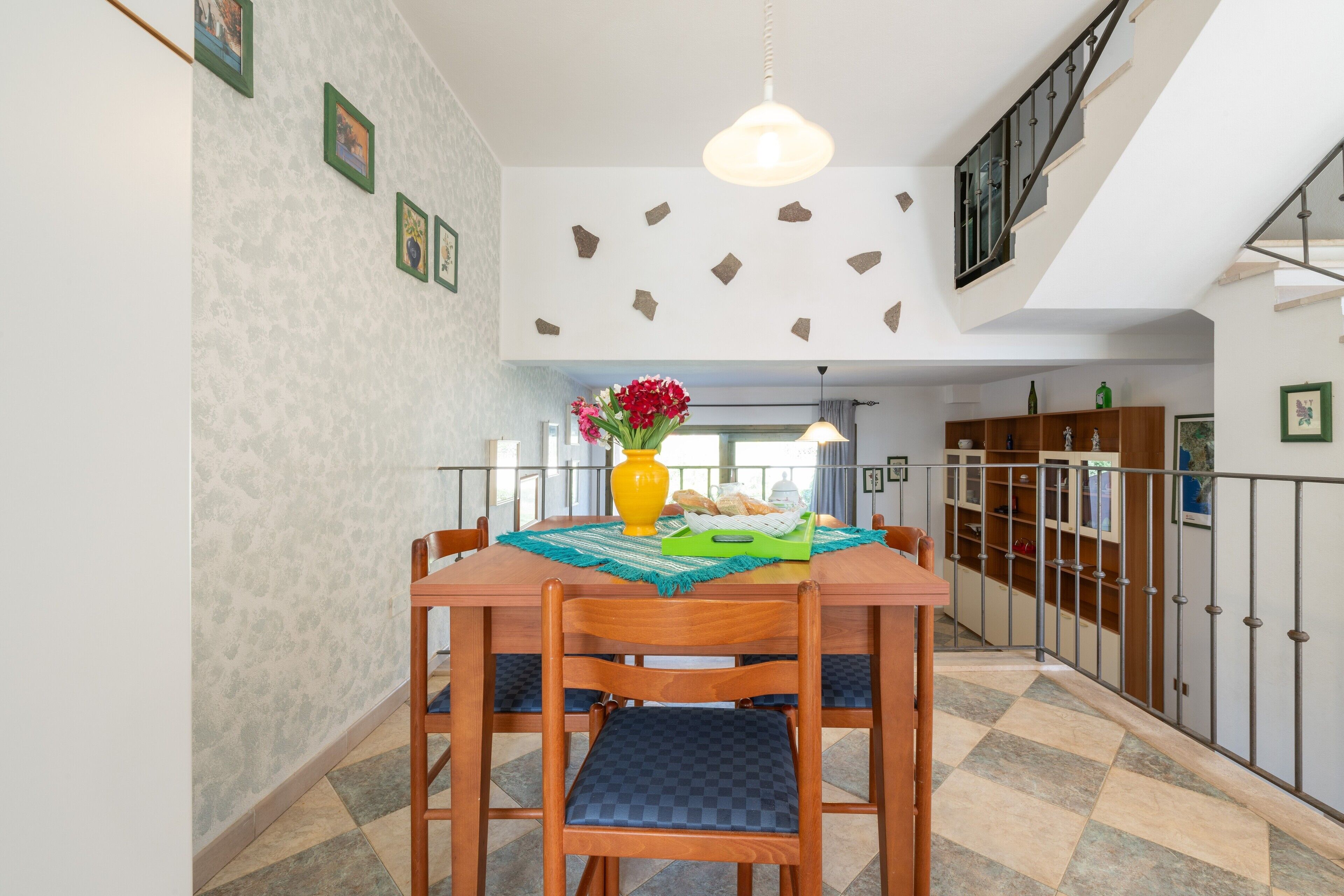 Un coin repas avec une table en bois, des chaises, un vase de fleurs et un escalier menant à une mezzanine.