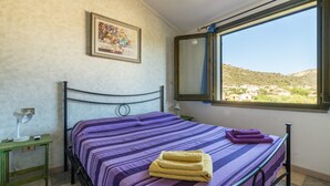 Un dormitorio con cama, una mesita de noche, una lámpara, un cuadro enmarcado y un ventanal con vistas al paisaje.