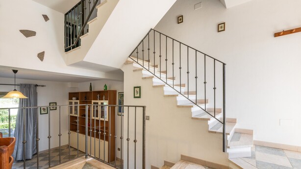 Un interior moderno con una escalera, barandilla de cristal y piso a cuadros.
