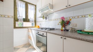 Cocina con armarios blancos, estufa a gas, ventana con cortinas y posavasos de Heineken.