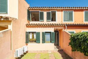 Un bâtiment à deux étages avec des volets verts, un toit en tuiles et un petit jardin.