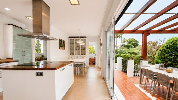 A modern kitchen with a central island, a dining area with a patio view, and a large glass door leading to an outdoor space. - Villa 'Gran Cerca De Puerto Banús' with Mountain Views, Wi-Fi, and Air Conditioning (Marbella)